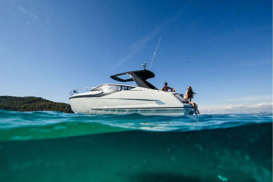 A sleek white motorboat in clear blue water with two people relaxing on the side, under a sunny sky.